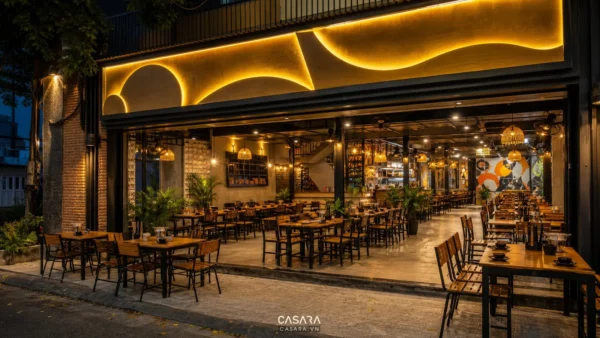 Quán nhậu độc lạ có mặt tiền mở, bàn ghế gỗ kim loại, biển hiệu nổi bật, ánh sáng vàng và không gian ăn uống buổi tối