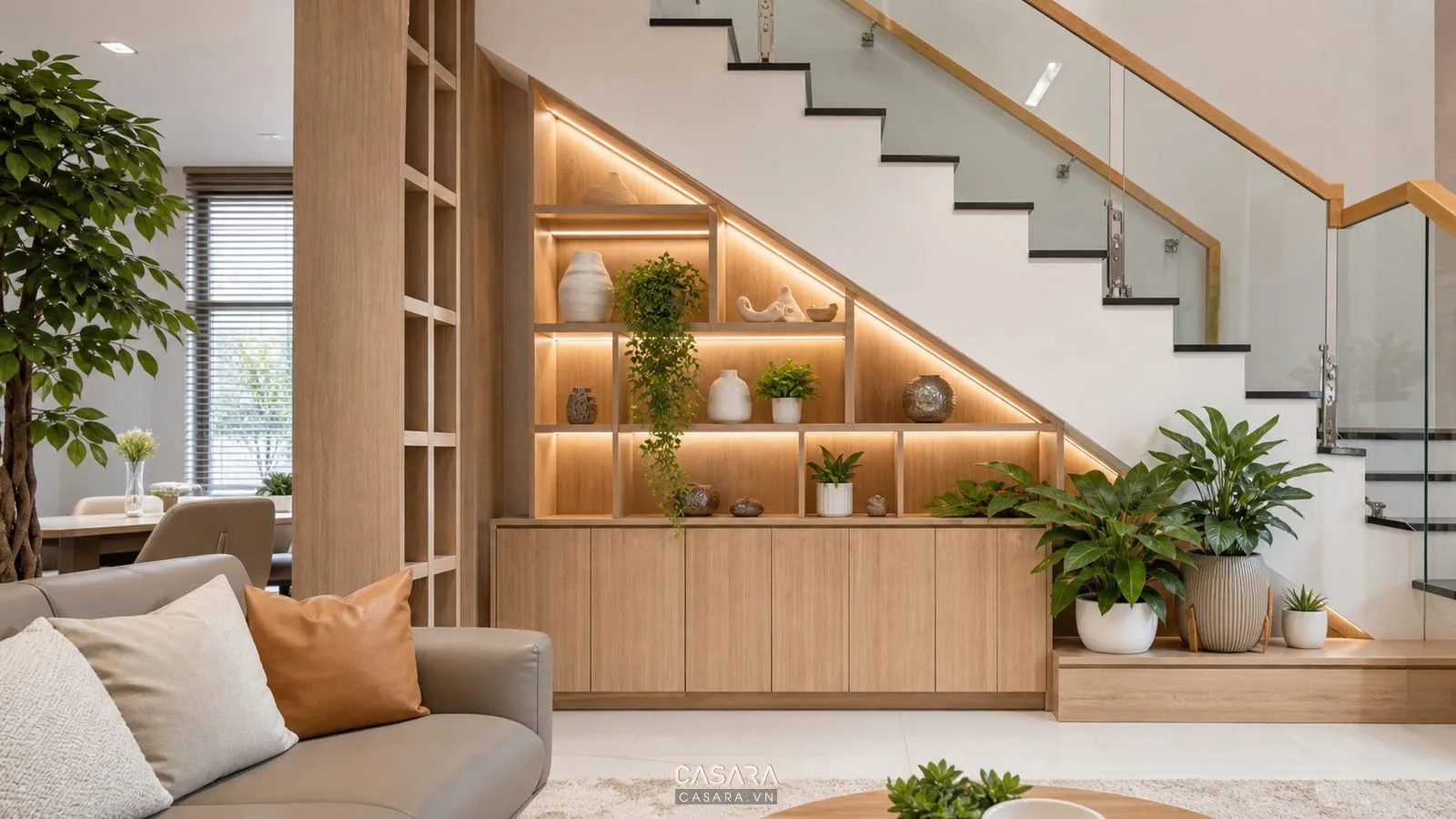 Tủ trang trí dưới gầm cầu thang kết hợp cây xanh với tủ gỗ sáng, kệ mở, chậu cây nội thất, phòng khách hiện đại và đèn led âm kệ