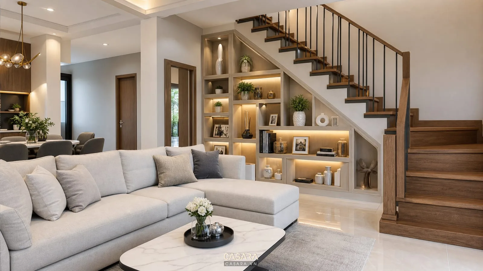 Trang trí dưới cầu thang phòng khách nhà phố hiện đại với sofa trung tính, cầu thang gỗ, kệ âm tường và đèn hắt ấm