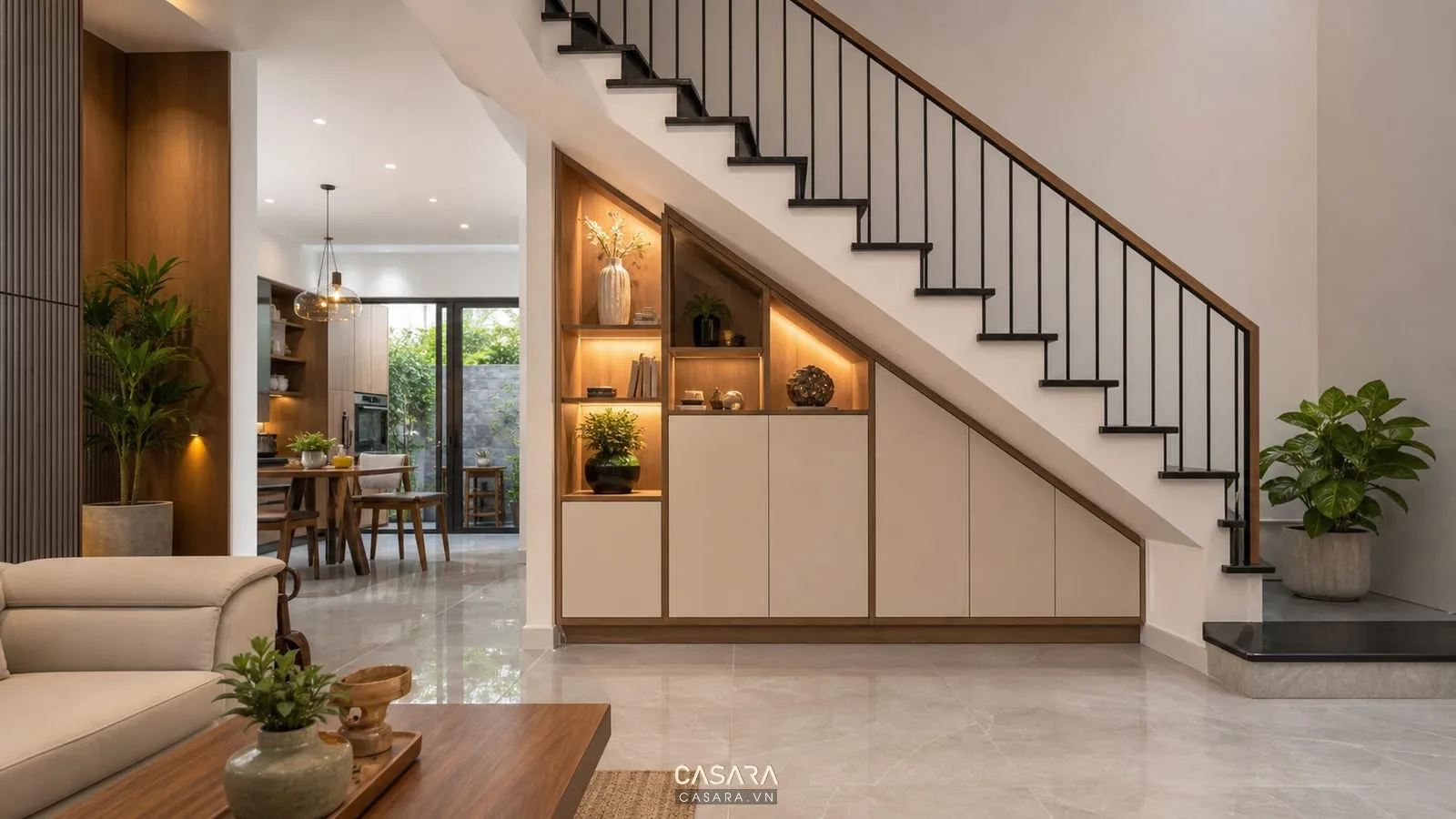 trang trí gầm cầu thang nhà ống bằng tủ âm, kệ gỗ, đèn hắt và cây xanh trong phòng khách
